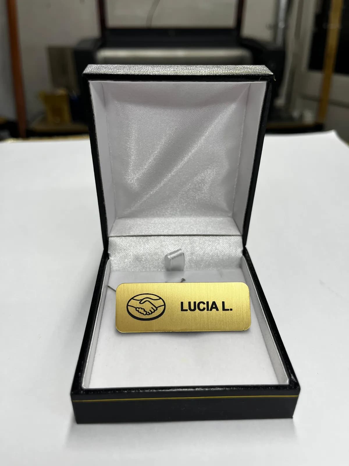 Credencial dorada grabada con un nombre, presentada en su caja de regalo