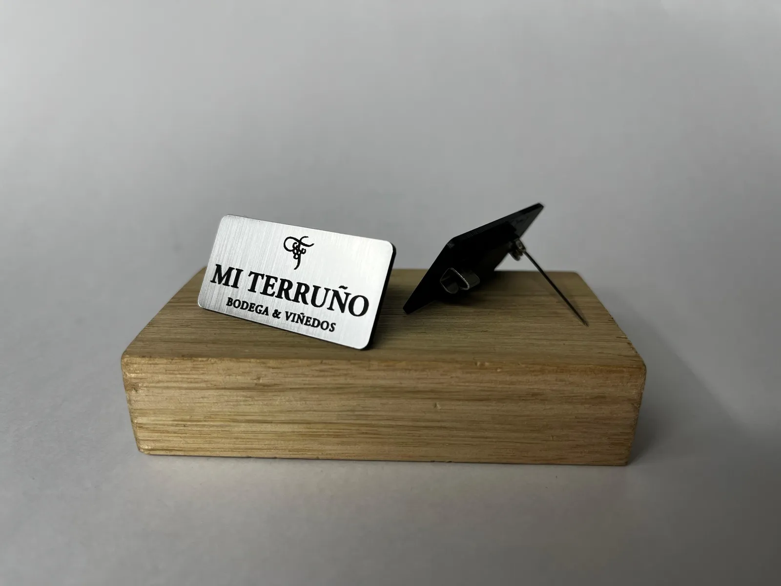 Credencial de metal plateado grabada con el logo de la bodega Mi Terruño, apoyada sobre un taco de madera