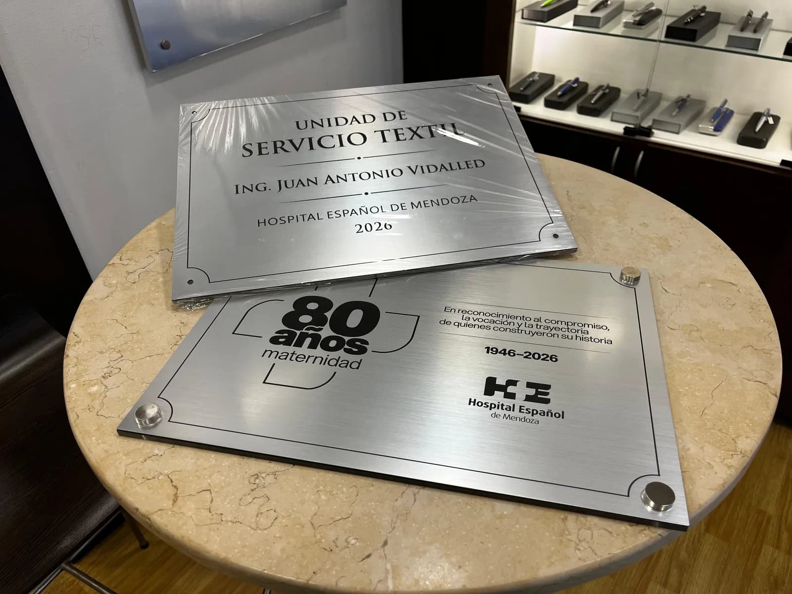 Placas institucionales de aluminio grabadas, apoyadas sobre una mesa