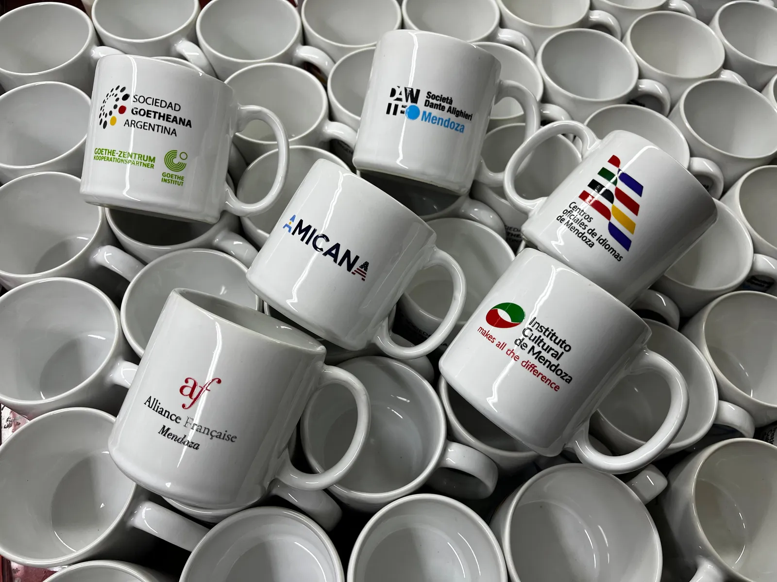 Tazas de cerámica blancas con los logos de institutos de idiomas de Mendoza