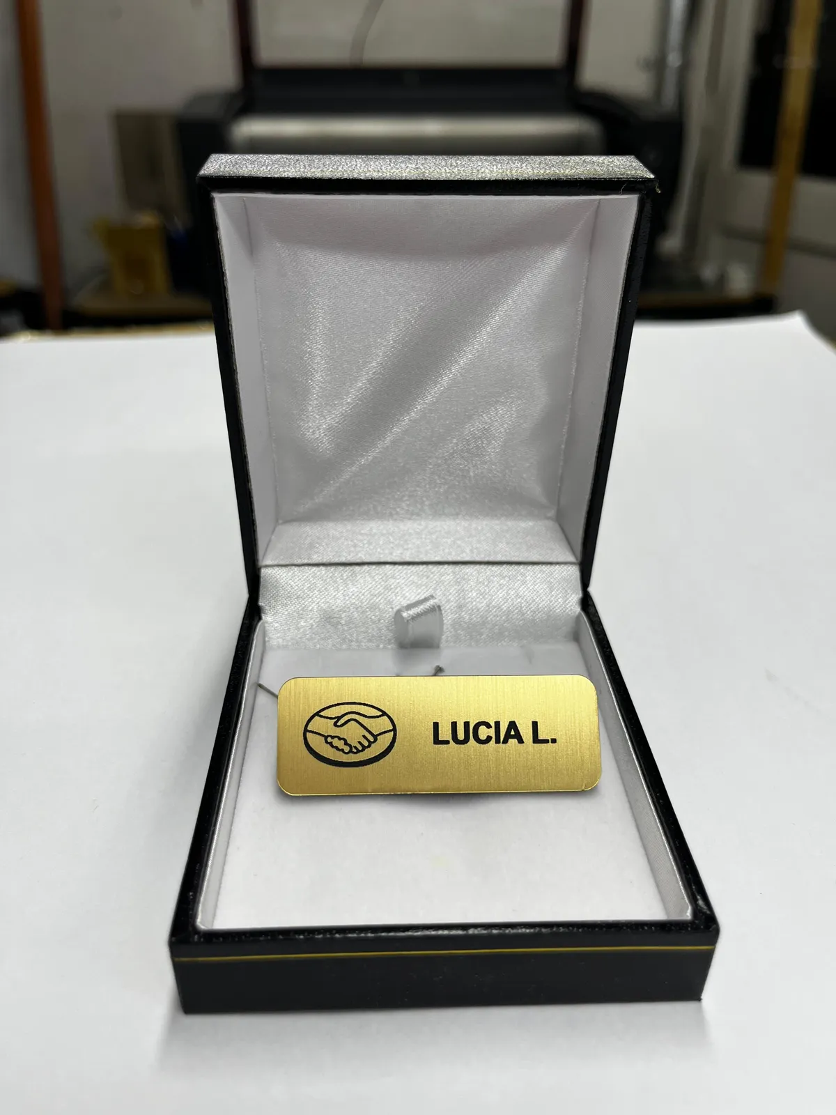 Credencial dorada grabada con un nombre, presentada en su caja de regalo