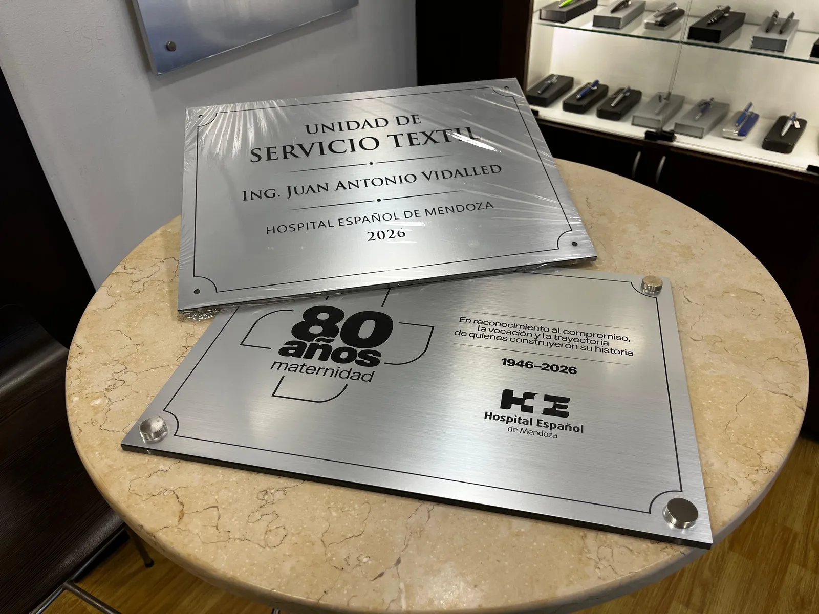 Placas institucionales de aluminio grabadas, apoyadas sobre una mesa
